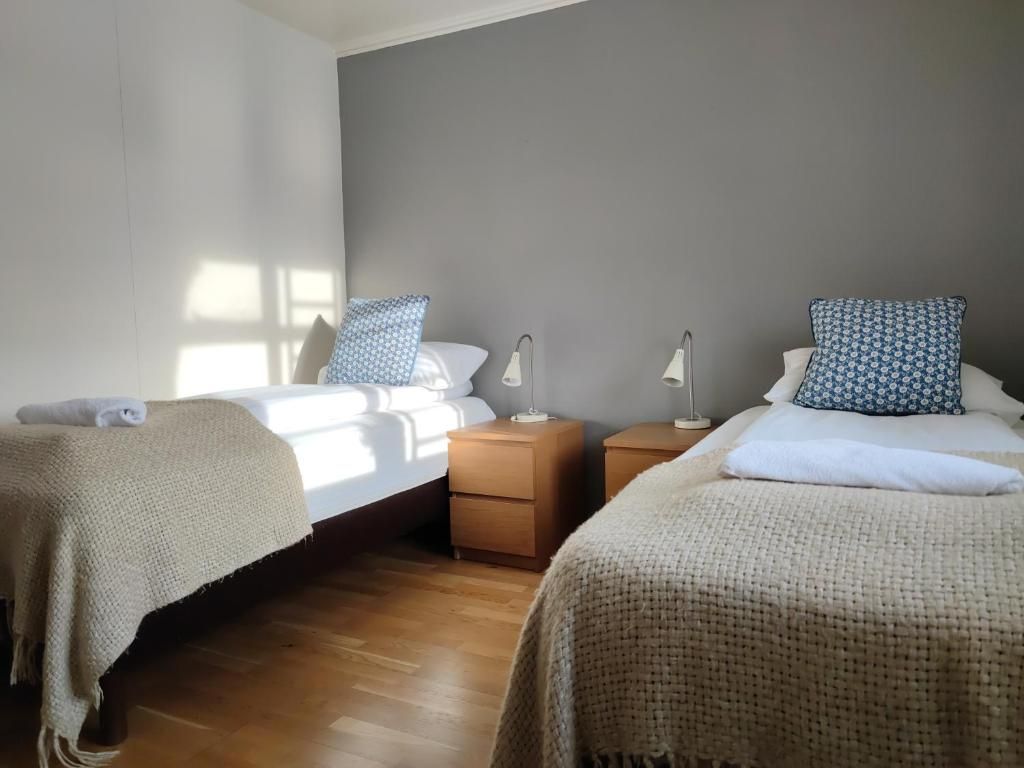 A bedroom with two beds, wooden nightstands, and bedside lamps.
