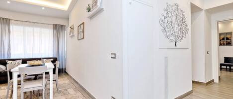A modern living room with a white sofa, a dining table with chairs, and a decorative wall art piece.