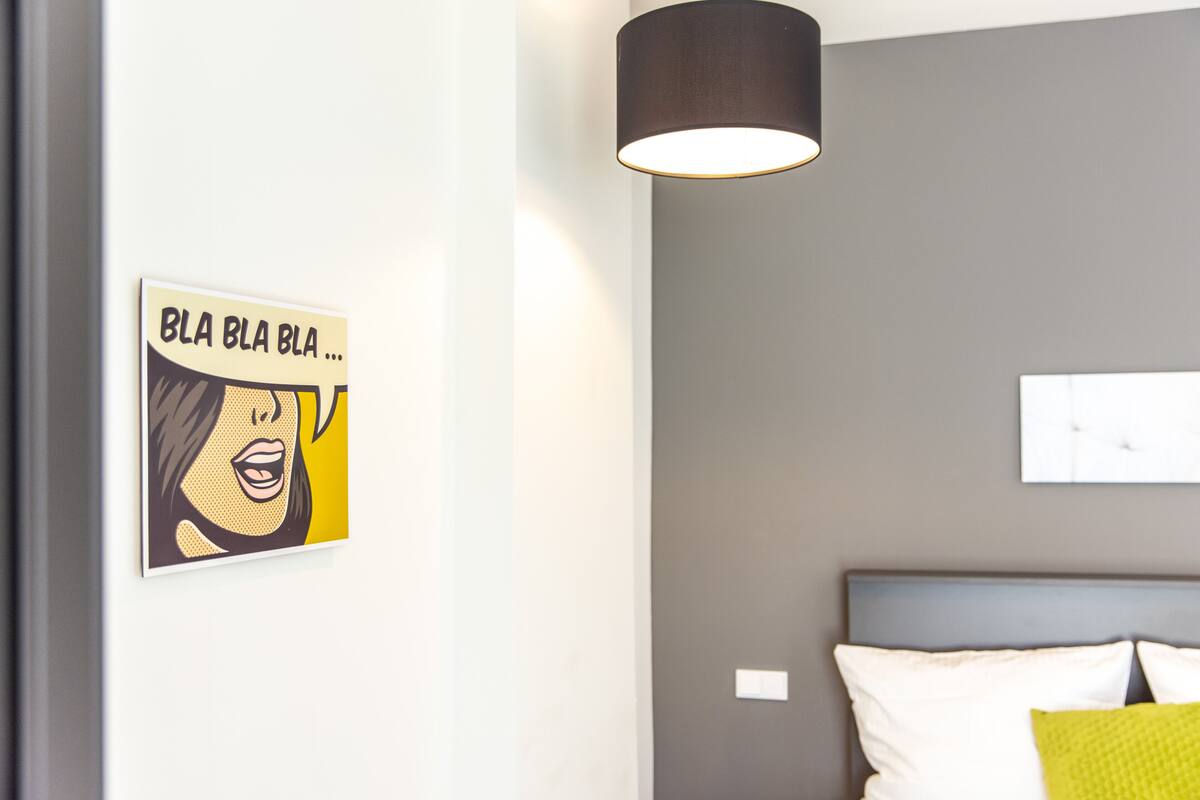 A bedroom with a bed, a wall-mounted light fixture, and a piece of artwork.