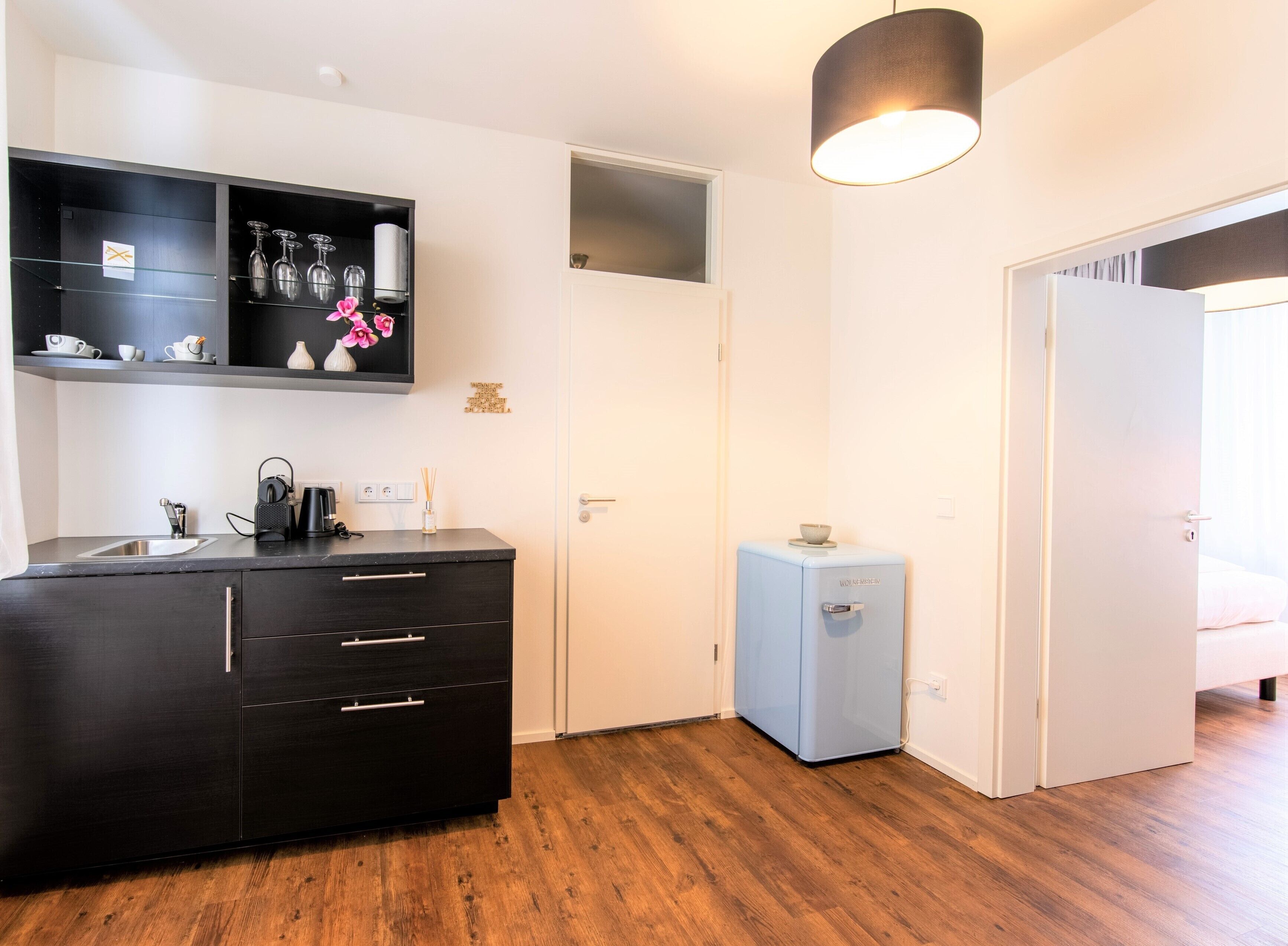 Une chambre d’hôtel moderne dotée d’un mini-bar noir, d’un petit réfrigérateur, d’un lavabo et d’un plancher en bois.