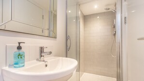 A bathroom with a white sink, a mirror, and a glass shower enclosure. - Black Lion (Surbiton)