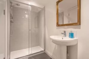 Une salle de bain avec une douche à parois de verre, un lavabo blanc et un miroir encadré d’or.