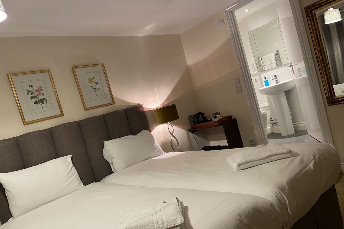 A hotel room with a large bed, two pillows, a bedside table with a lamp, and a mirror above the sink.