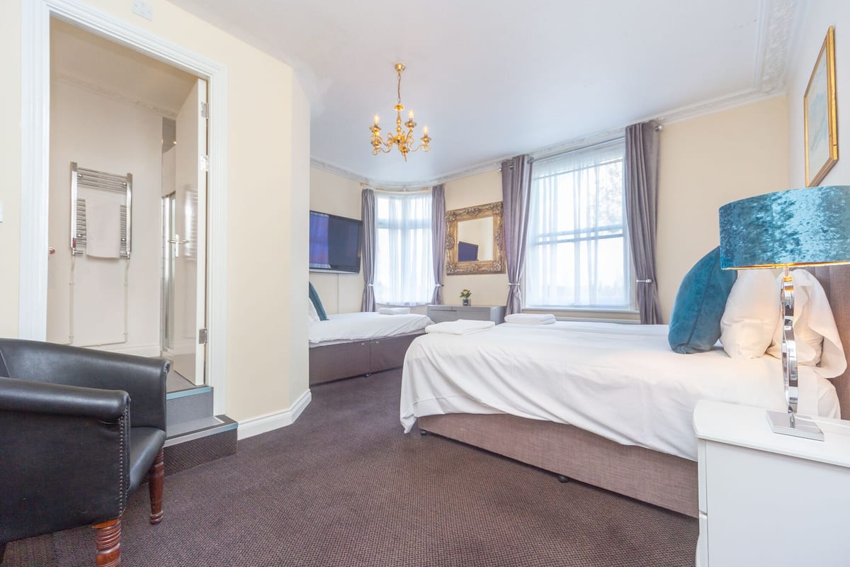 A hotel room with a large bed, a desk with a lamp, a chair, a mirror, and a chandelier.