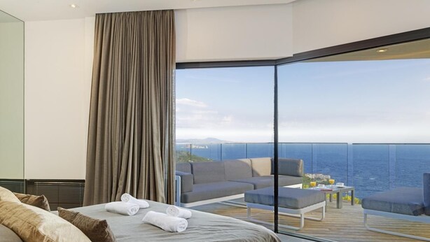 Een moderne hotelkamer met een groot bed, een balkon met uitzicht op zee en een zithoek met een tafel en stoelen.