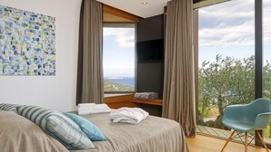Een moderne slaapkamer met een groot bed, uitzicht op het landschap en een aan de muur bevestigde televisie.
