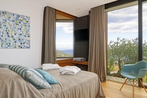 A modern bedroom with a large bed, a view of the landscape, and a TV mounted on the wall. - Holiday rental villa with swimming pool in Begur, Sa Tuna (Begur)