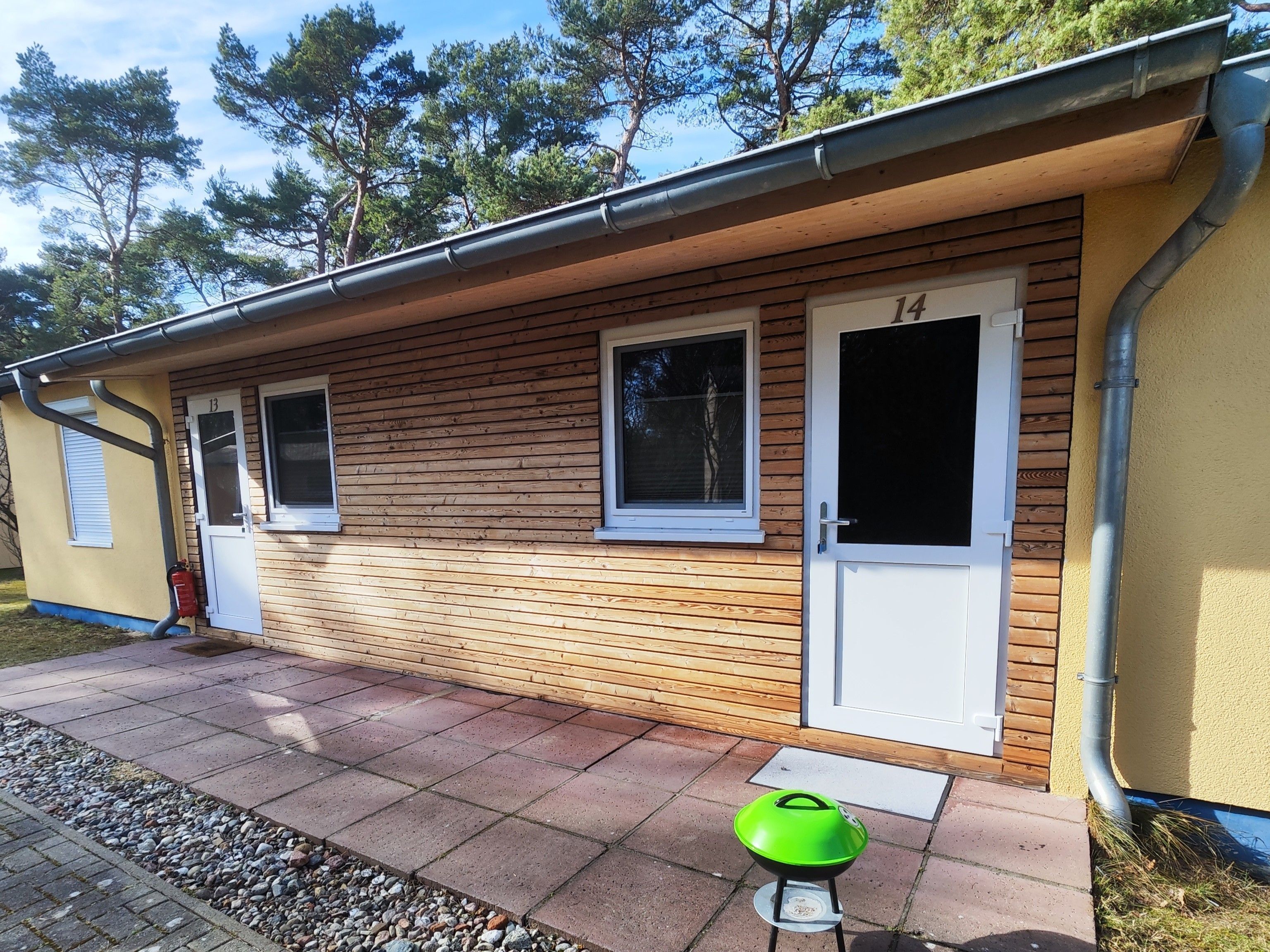 Ein Holzhaus mit der Türnummer 14, einem Fenster und einem kleinen Grillplatz.