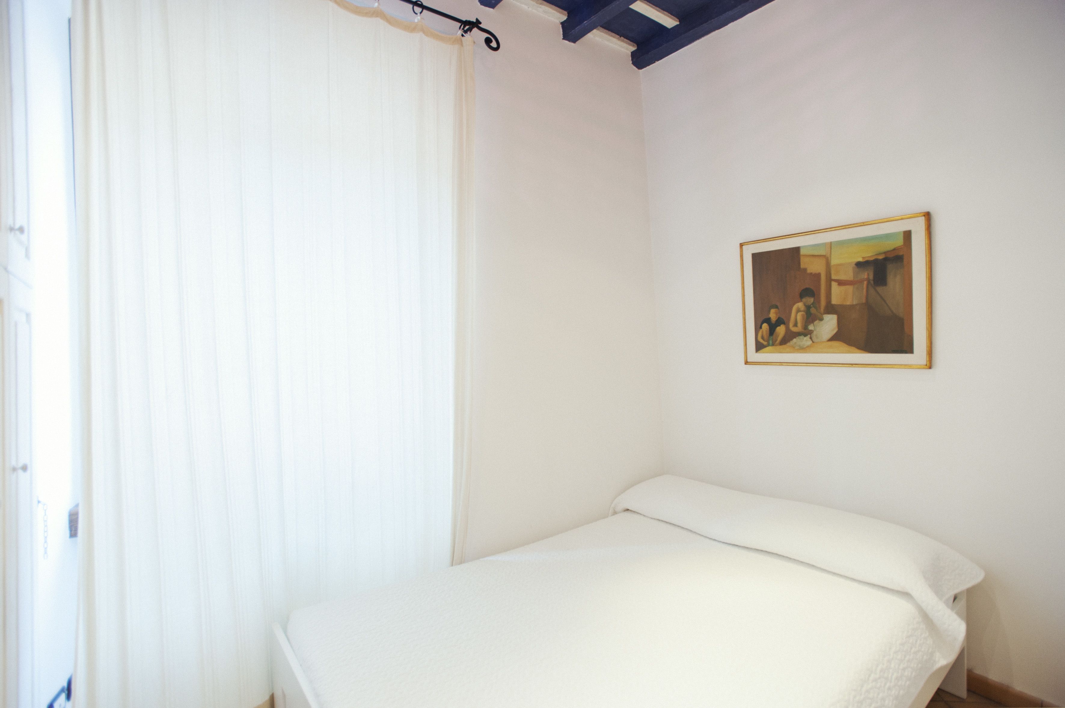 A single bed in a room with a white wall and a painting.