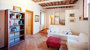 A cozy living room with a white sofa, a red ottoman, and a wooden bookshelf. - Lungaretta 2 - WR Apartments (Rome)