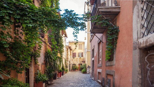 A narrow cobblestone street flanked by buildings with ivy-covered walls and potted plants. - Lungaretta 2 - WR Apartments (Rome)