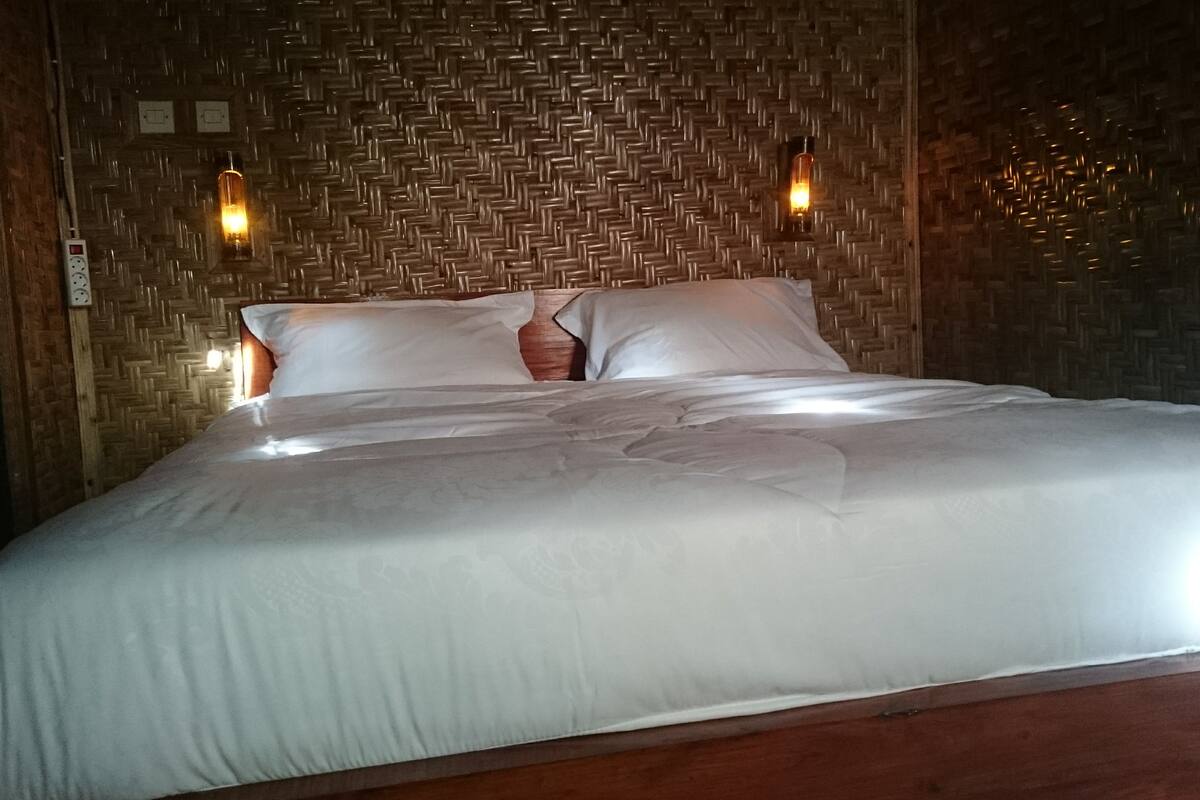A neatly made bed with white linens in a room with a woven wall pattern and two wall-mounted lights.