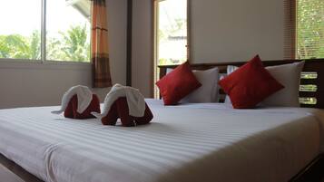 Une chambre d’hôtel avec un grand lit, des oreillers rouges et blancs, et une fenêtre avec des stores.