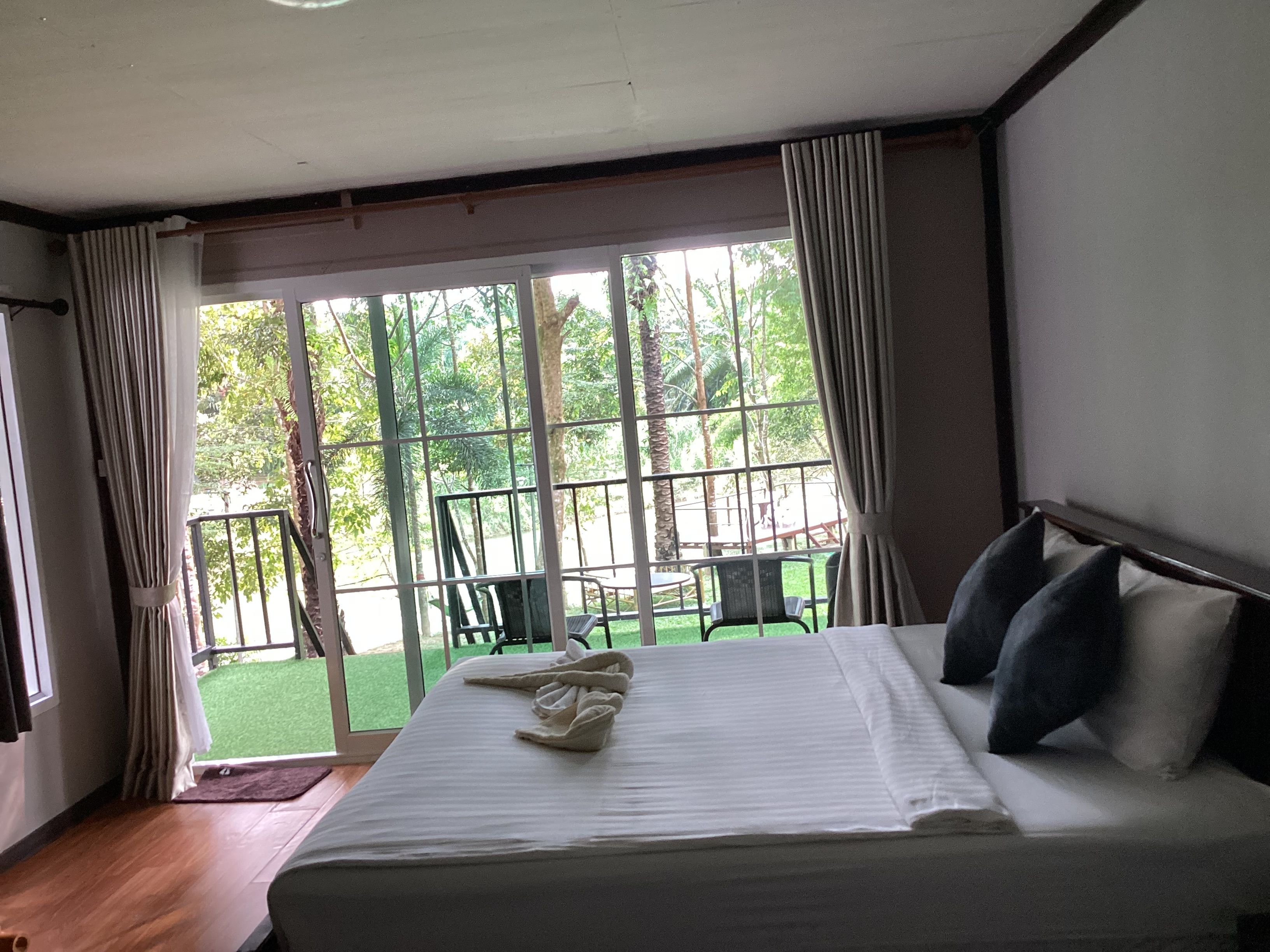 Een hotelkamer met een groot bed, uitzicht op het landschap door een raam, en een balkon met stoelen.