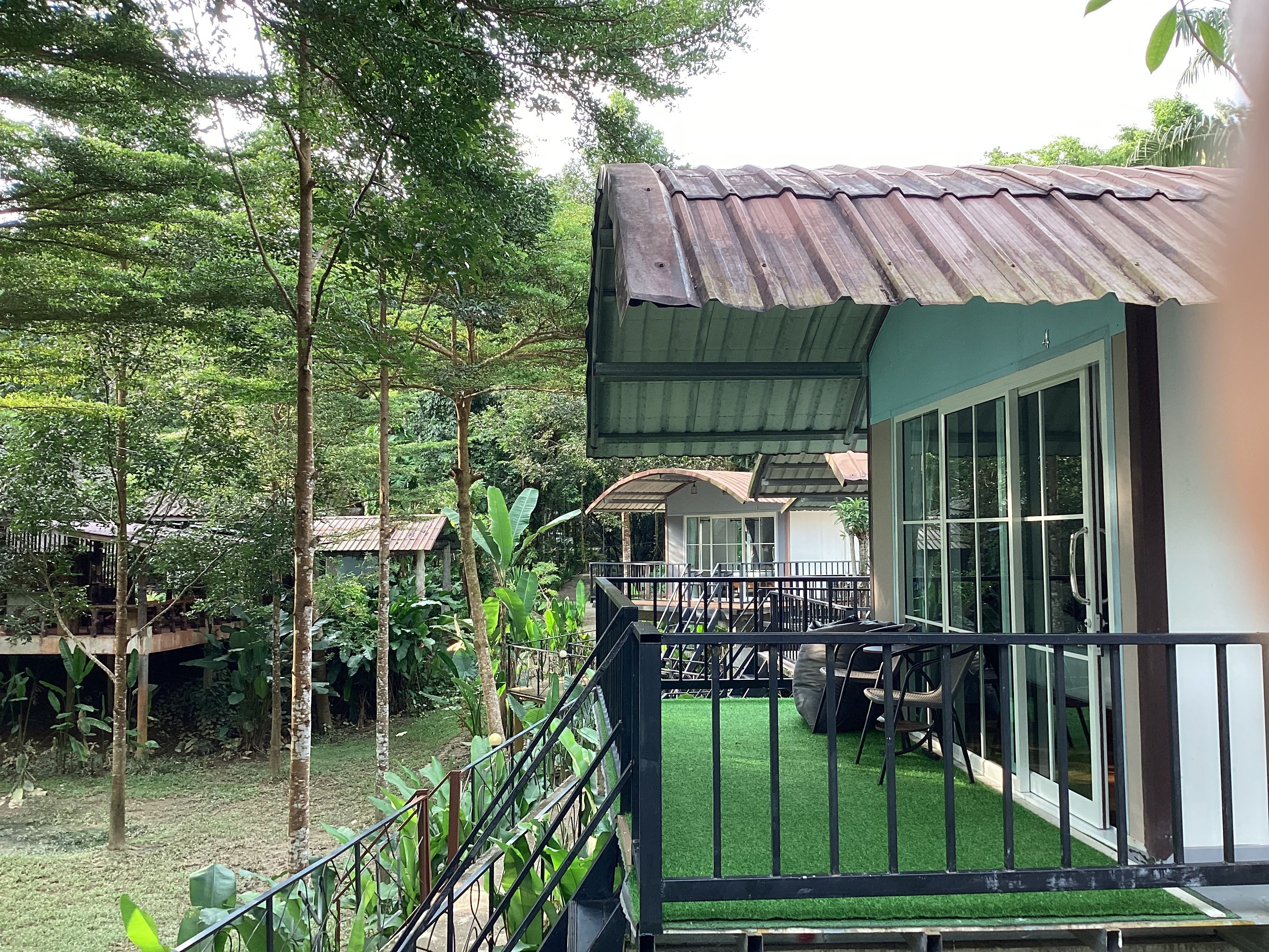 A building with a covered porch, a staircase, and a view of a lush garden.