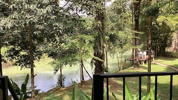 Vista de un río con árboles y una terraza de madera con sillas.