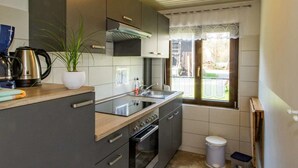 A compact kitchen with a built-in oven, a sink, and a window with a view of the outdoors. - Ferienhof Bohg (Burg (Spreewald))