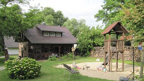 A rustic house with a stone chimney, a wooden playhouse, and a well-maintained garden. - Ferienhof Bohg (Burg (Spreewald))