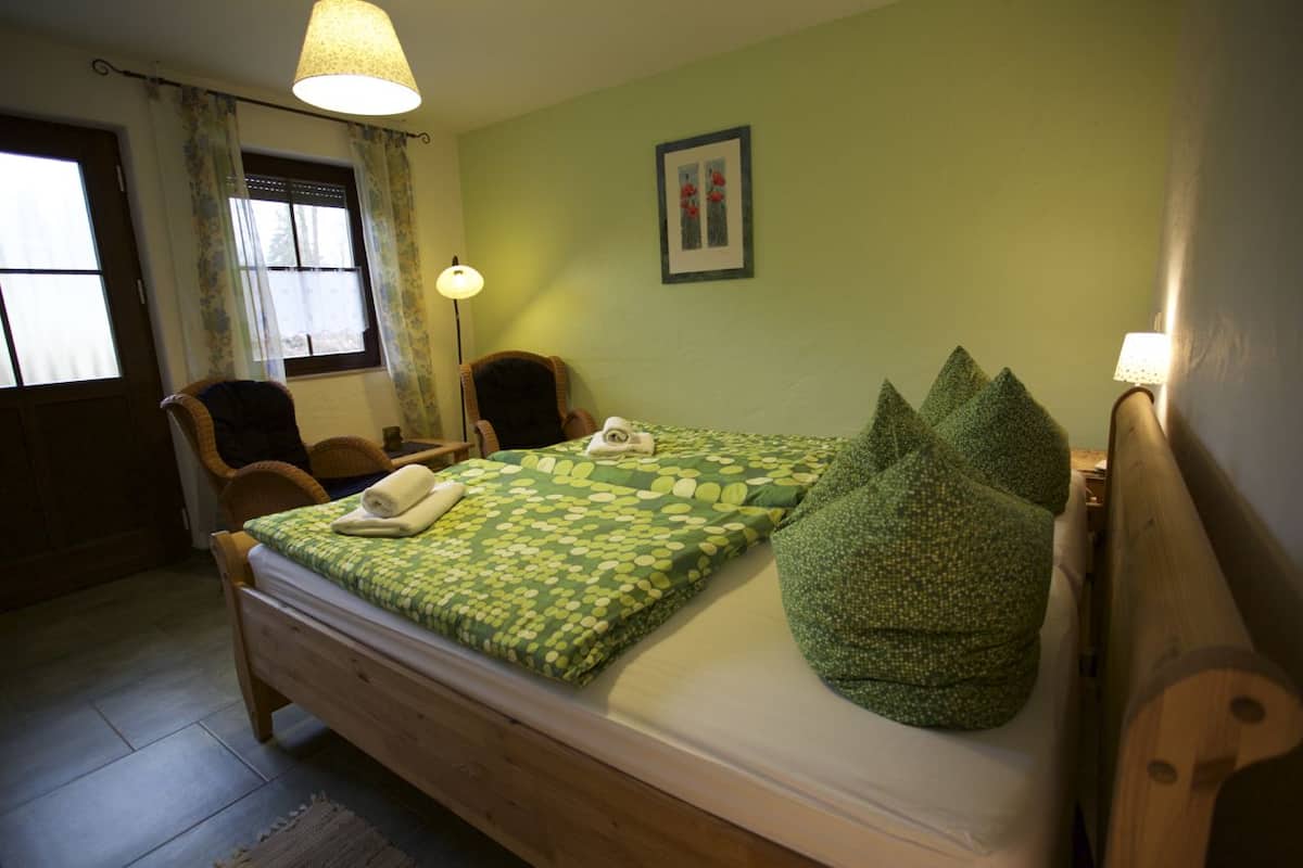 Ein Schlafzimmer mit einem hölzernen Bett, grüner Bettwäsche, einem Sessel, einem Schreibtisch und einer Lampe.