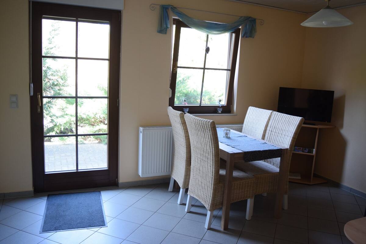 Ein Essbereich mit Tisch, Stühlen, einem Fernseher und einem fenster mit Vorhängen.