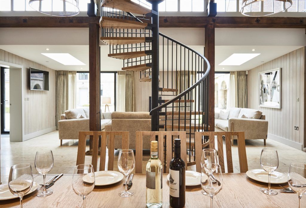 A dining area with a wooden table set for a meal, a spiral staircase, and a view of the living room.