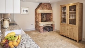 A kitchen with a brick fireplace, a granite countertop, and a wooden cabinet with glass doors. - Chesters Stables (Hexham)