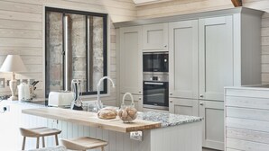 A modern kitchen with a central island, built-in appliances, and wooden paneling. - Chesters Stables (Hexham)