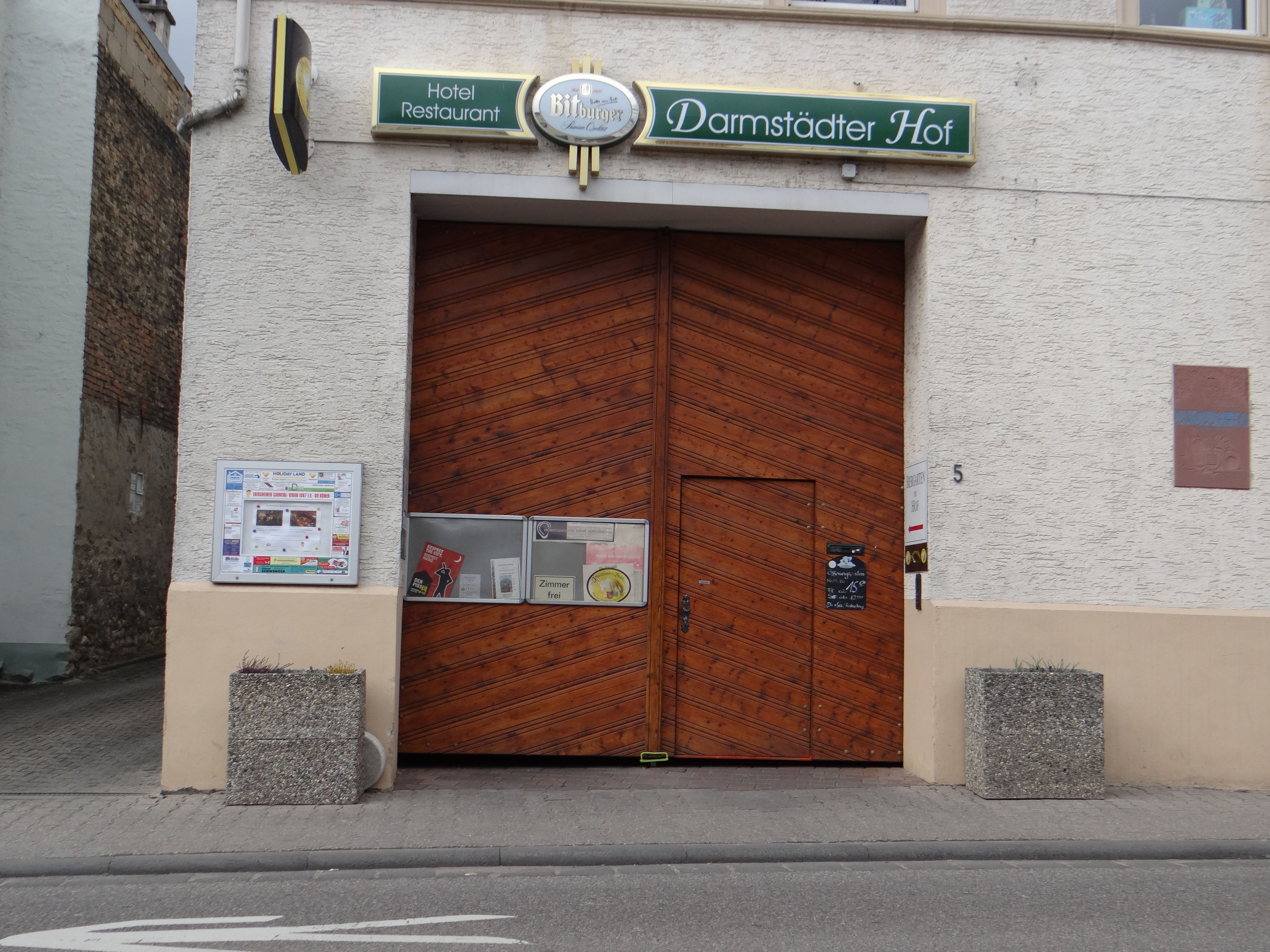 Entrada de un hotel con una gran puerta de madera, un cartel que indica que es un hotel y restaurante, y un pequeño letrero debajo de la puerta anunciando un descuento del 15%.