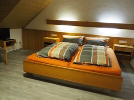 Habitación individual con una cama de madera, dos mesitas de noche y un televisor sobre un mueble bajo.