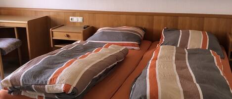 Una cama individual con cabecera de madera, una mesita de noche y una silla.