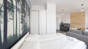 Een moderne hotelkamer met een groot bed, een grijze bank, een houten accentmuur en een keuken in de achtergrond.