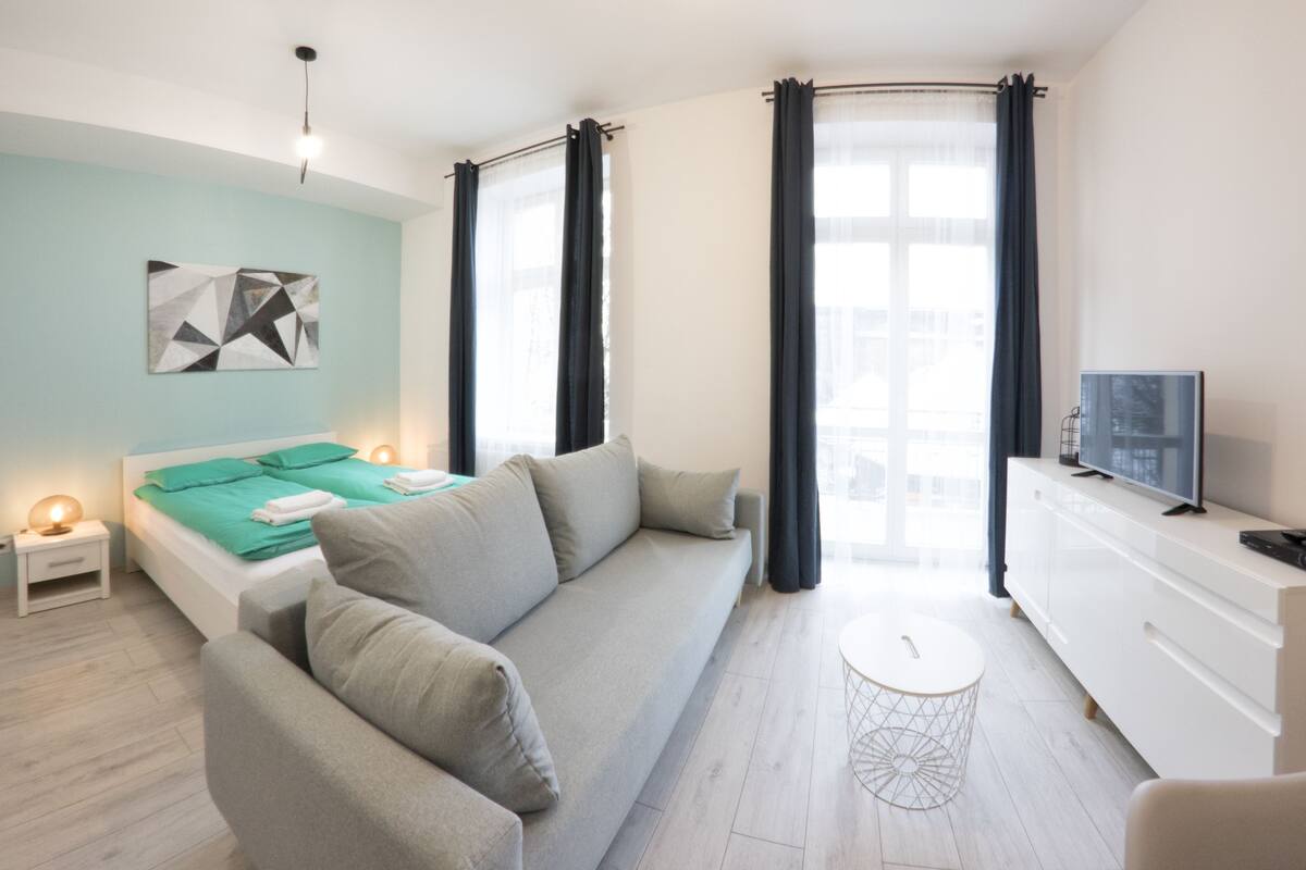 Um quarto moderno com cama, sofá, televisão e uma mesinha.