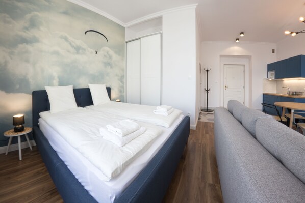 A modern bedroom with a large bed, a sofa, a dining area, and a coat rack.