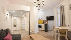 Een modern appartement met een woonkamer, eethoek, keuken en een trap naar een verdieping erboven.