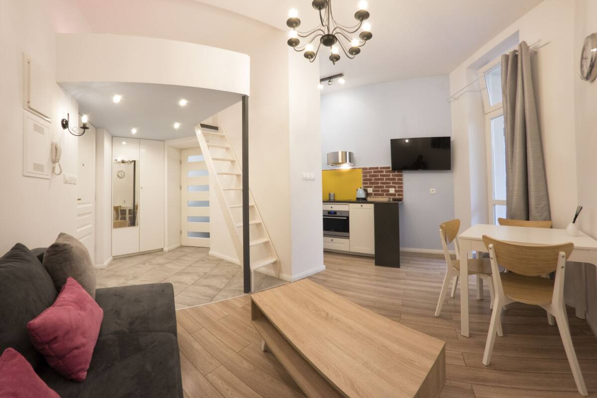 Um apartamento moderno com sala de estar, área de jantar, cozinha e uma escada que leva a um andar superior.