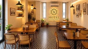 Interior d'hotel amb diverses taules i cadires per dinar, un paviment amb dibuixos i una paret central amb un logotip i un nom.