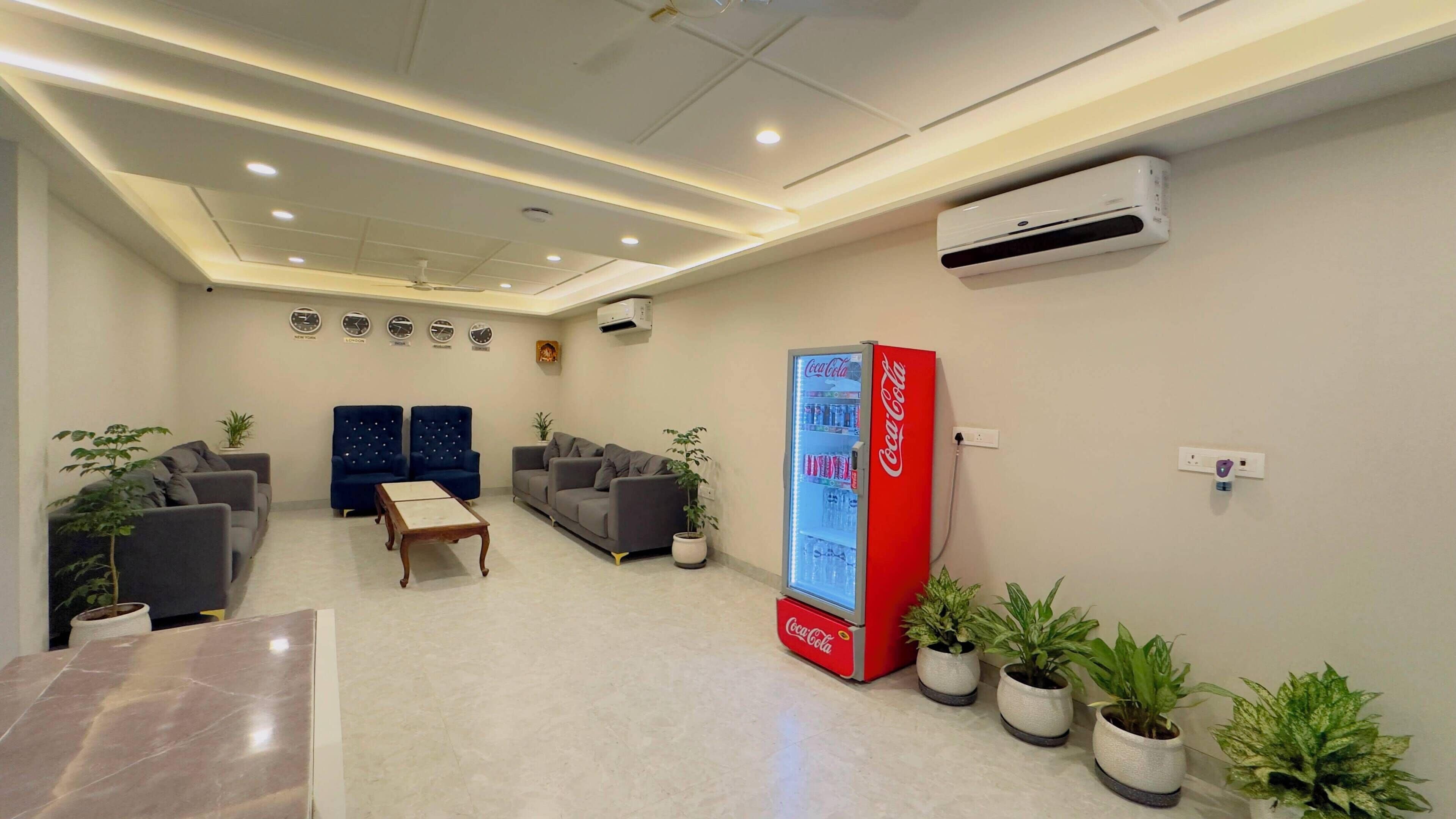 Een hotel lobby met zitplaatsen, een Coca-Cola koelkast en een airconditioningsunit.