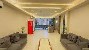 Um hall de hotel com uma mesa de recepção, dois sofás, um refrigerador de Coca-Cola e uma parede decorativa.