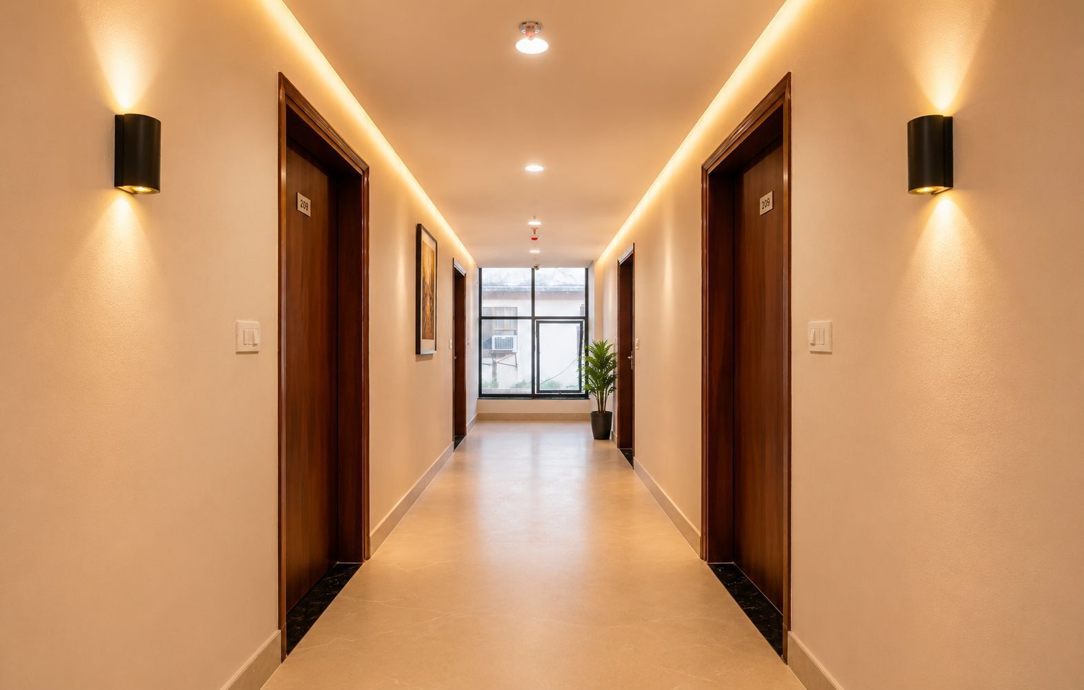Un couloir d’hôtel avec des portes en bois, des lampes fixées au mur et une plante en pot.