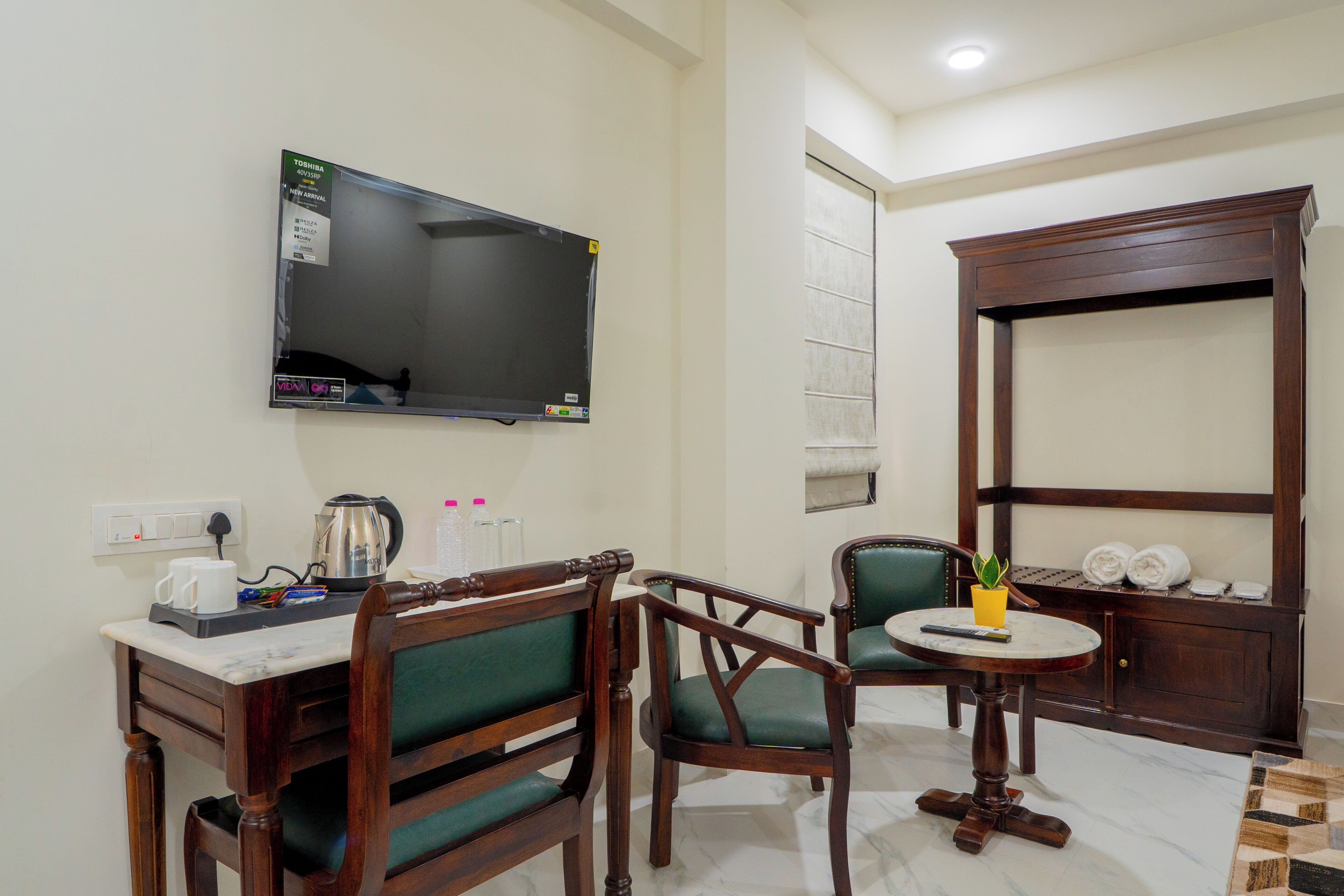 A room with a TV, a coffee maker, a table with chairs, and a cabinet with towels.