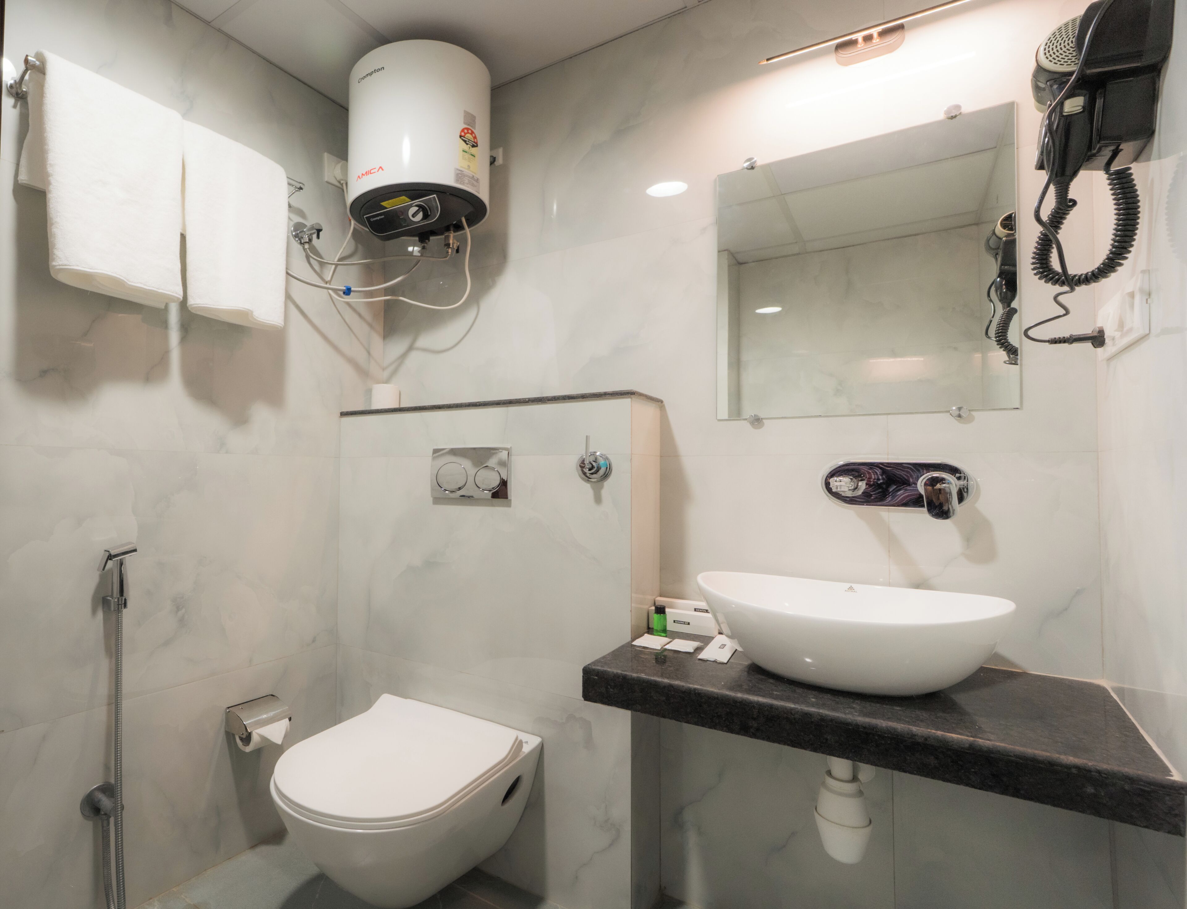 A modern bathroom with a toilet, sink, mirror, hairdryer, and a water heater.