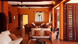 A spacious living area with a sofa, a coffee table, and a fireplace. There is a window with a decorative grille and a door with a wooden lattice design. - Sunset Villa Resort (Diani Beach)
