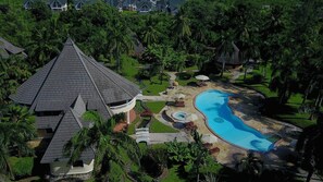 Une grande maison avec une piscine, entourée d’une végétation luxuriante et de palmiers.