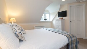 Un dormitorio con cama, mesita de noche, lámpara, cómoda, televisor y ventana.