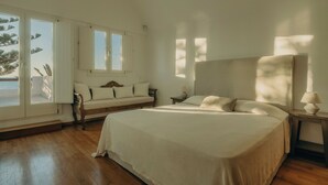 A bedroom with a large bed, a wooden bench, a nightstand, and a window with a view of the outdoors. - Damma Beachfront Luxury Villa (Santorini)