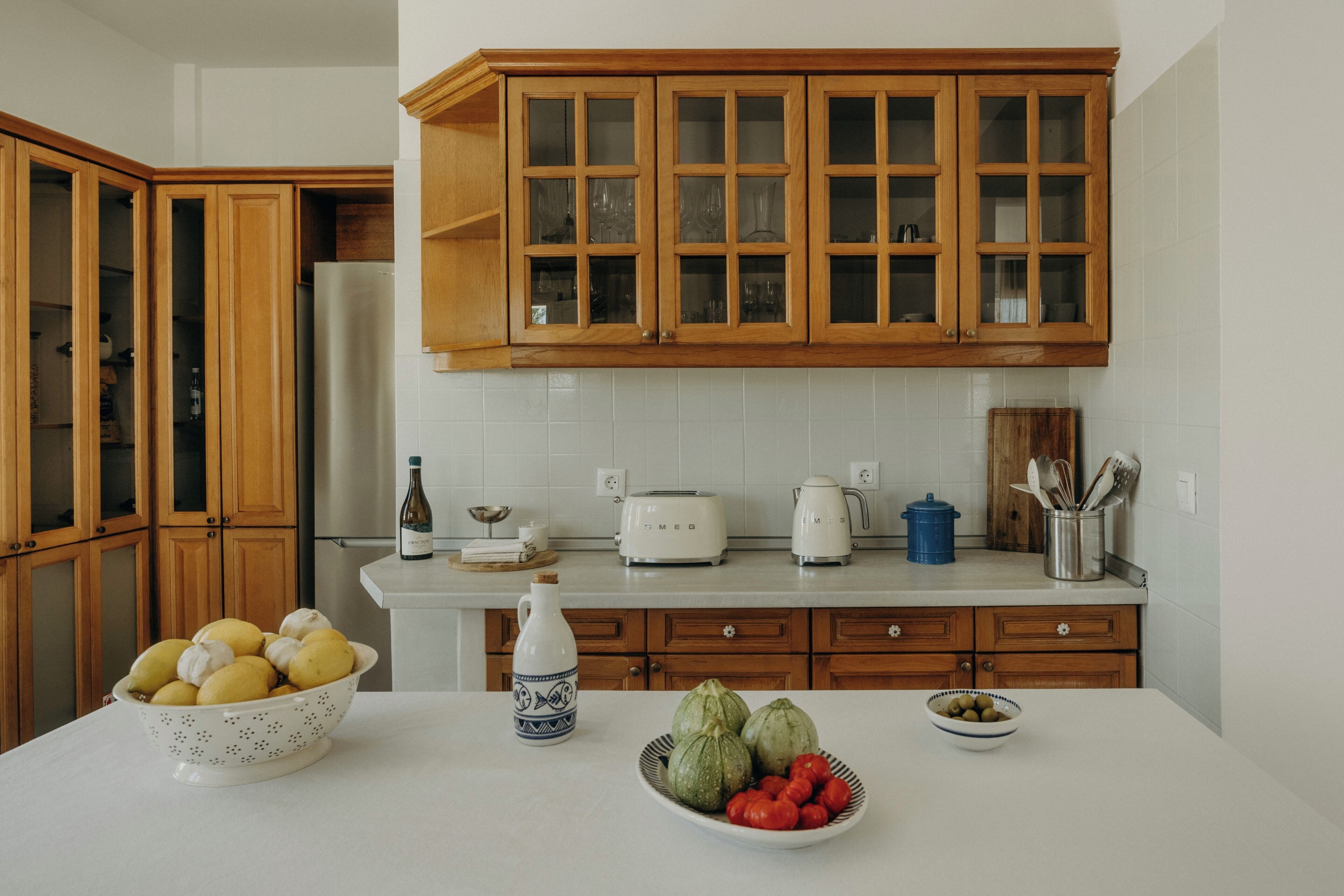 Eine Küche mit Holzausstattung, einem Edelstahlkühlschrank, einer weißen Arbeitsplatte und verschiedenen Küchengeräten.