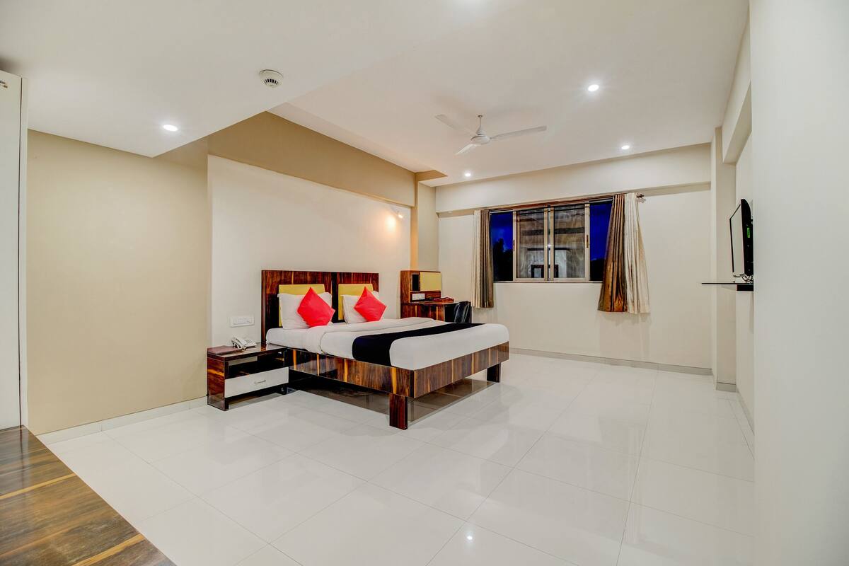 A modern bedroom with a large bed, bedside tables, a nightstand, a ceiling fan, a window with curtains, and a wall-mounted TV.