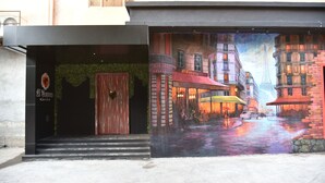 Fachada de edificio con un mural de una calle lluviosa, una puerta de madera y un letrero que dice 'El Cortez'.