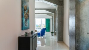 A modern hallway with a black console table, a blue chair, and a green door leading to a balcony with a view of buildings. - Blue Marlin - Famous Handelskade Apartment (Willemstad)