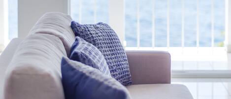 A modern living room with a sofa and large windows overlooking a body of water and buildings.